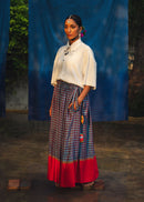 Woman wearing a white blouse and a colorful skirt with a blue curtain background
