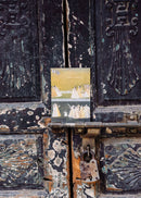 Vintage metal door with peeling paint and a small painting attached, featuring a landscape scene.